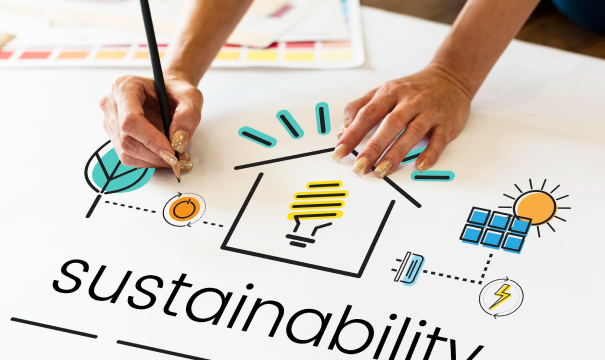 Hands drawing a diagram of sustainability elements. The diagram includes an energy-efficient house, a leaf, a sun with solar panels, and various eco-friendly icons. The word 