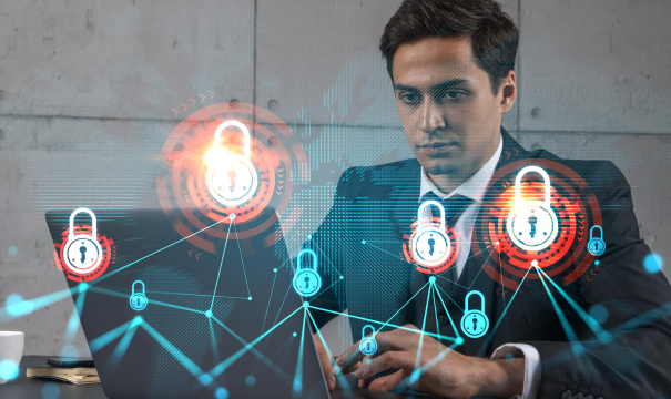 A man in a suit works on a laptop, with digital security graphics, such as glowing padlocks connected by lines, superimposed over the image, symbolizing cybersecurity and protection of information. The background shows a plain office wall.