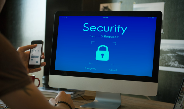 A person holding a smartphone sits in front of a computer monitor displaying a blue screen with the word 