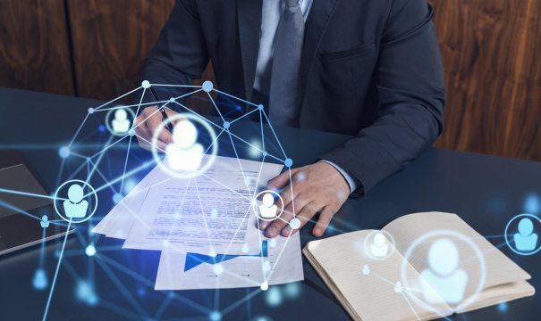 A person in a suit is seated at a desk, reviewing documents and a notebook. Several icons and interconnected lines are superimposed over the scene, suggesting a network or technological connections, indicating themes of business, communication, or networking.