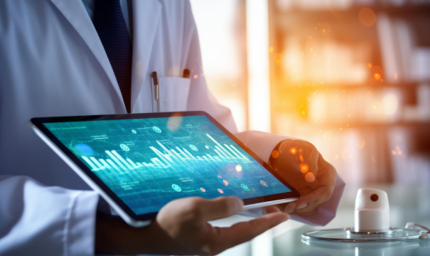 A person in a white lab coat holds a tablet displaying data visuals with charts and graphs. The background is softly blurred with office or laboratory equipment, and warm, glowing light effects add a dynamic feel to the scene.