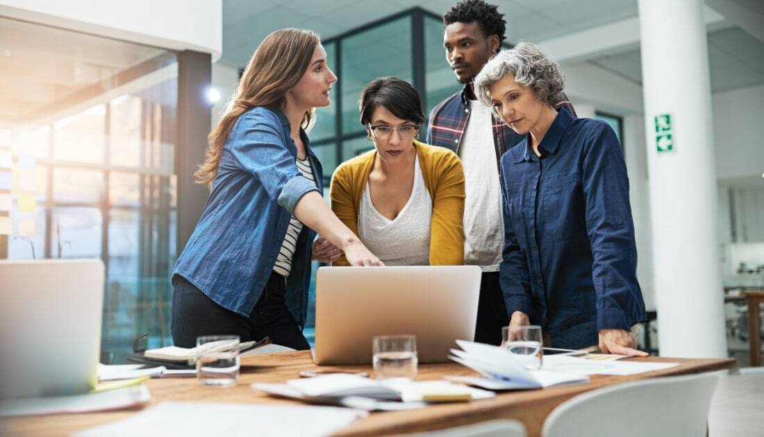 team of creative businesspeople Leveraging Power Platform updates around a laptop in the office