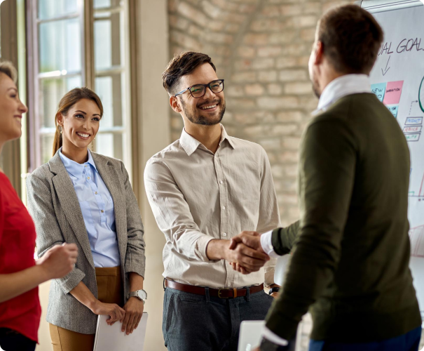 Two men shaking hands in office attire, with two women standing alongside.