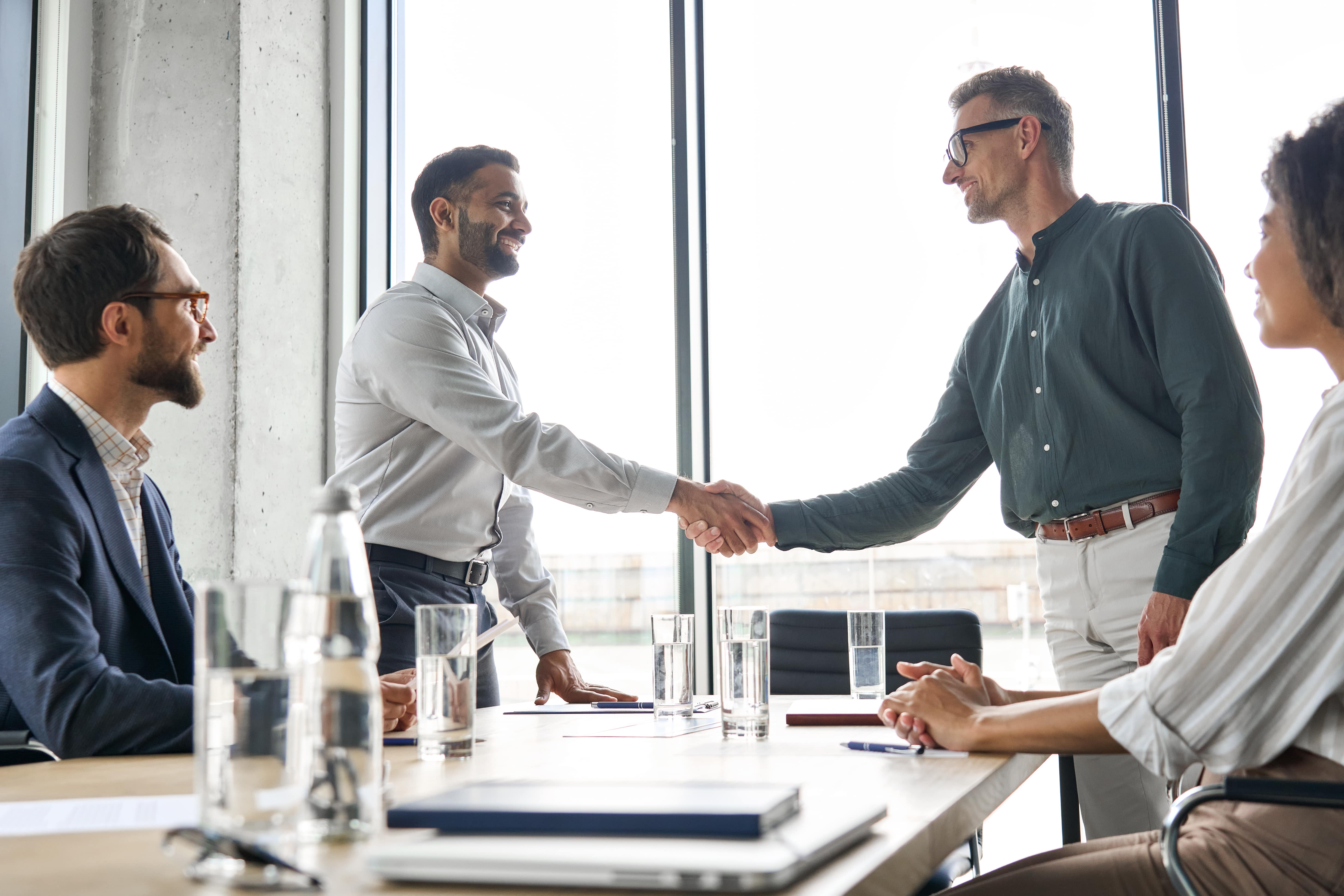 Business professionals in a modern office shaking hands across a conference table, symbolizing collaboration and trust—representing the long-standing DSI USC Consulting Group partnership focused on strategic execution and performance improvement.